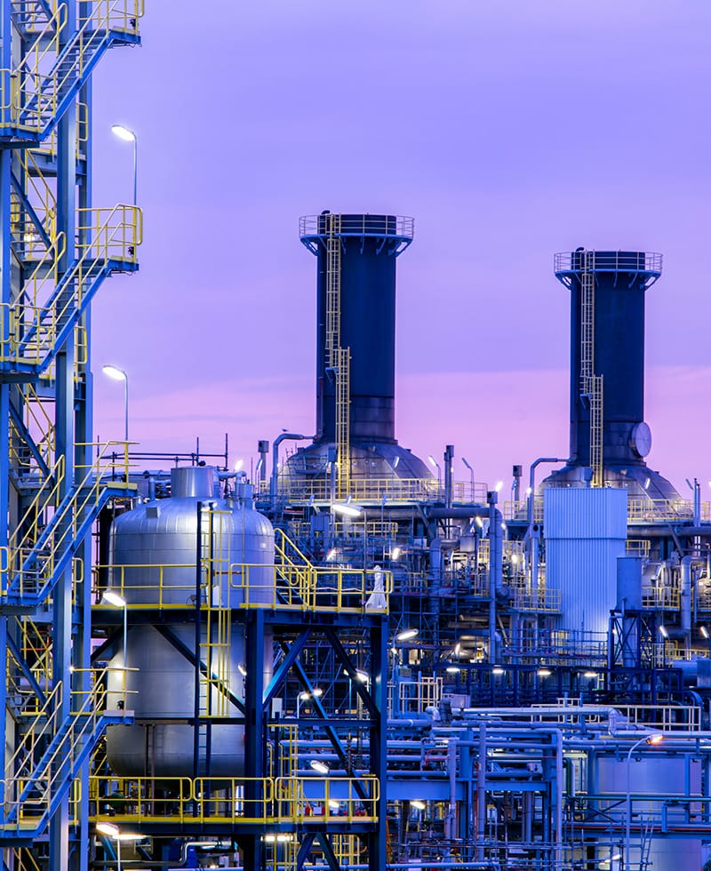 Large industrial facility with towers, tanks, and pipes at dusk.